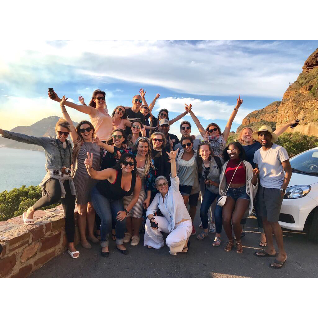 Group of travelers celebrating together at a scenic overlook on the Cape Town coastline during an Unsettled retreat